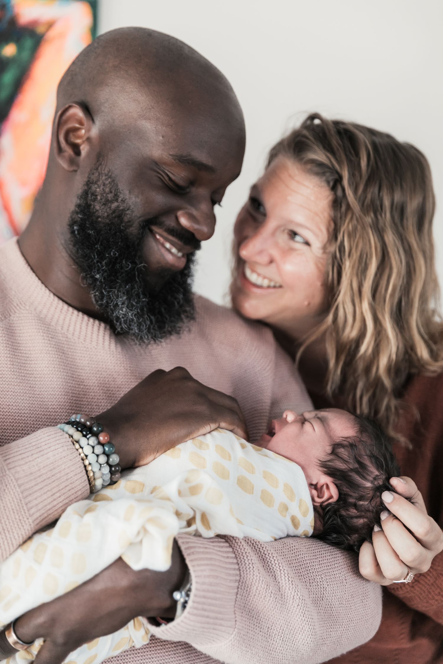 A tender moment as new parents gaze lovingly at their newborn baby swaddled in a polka dot blanket.