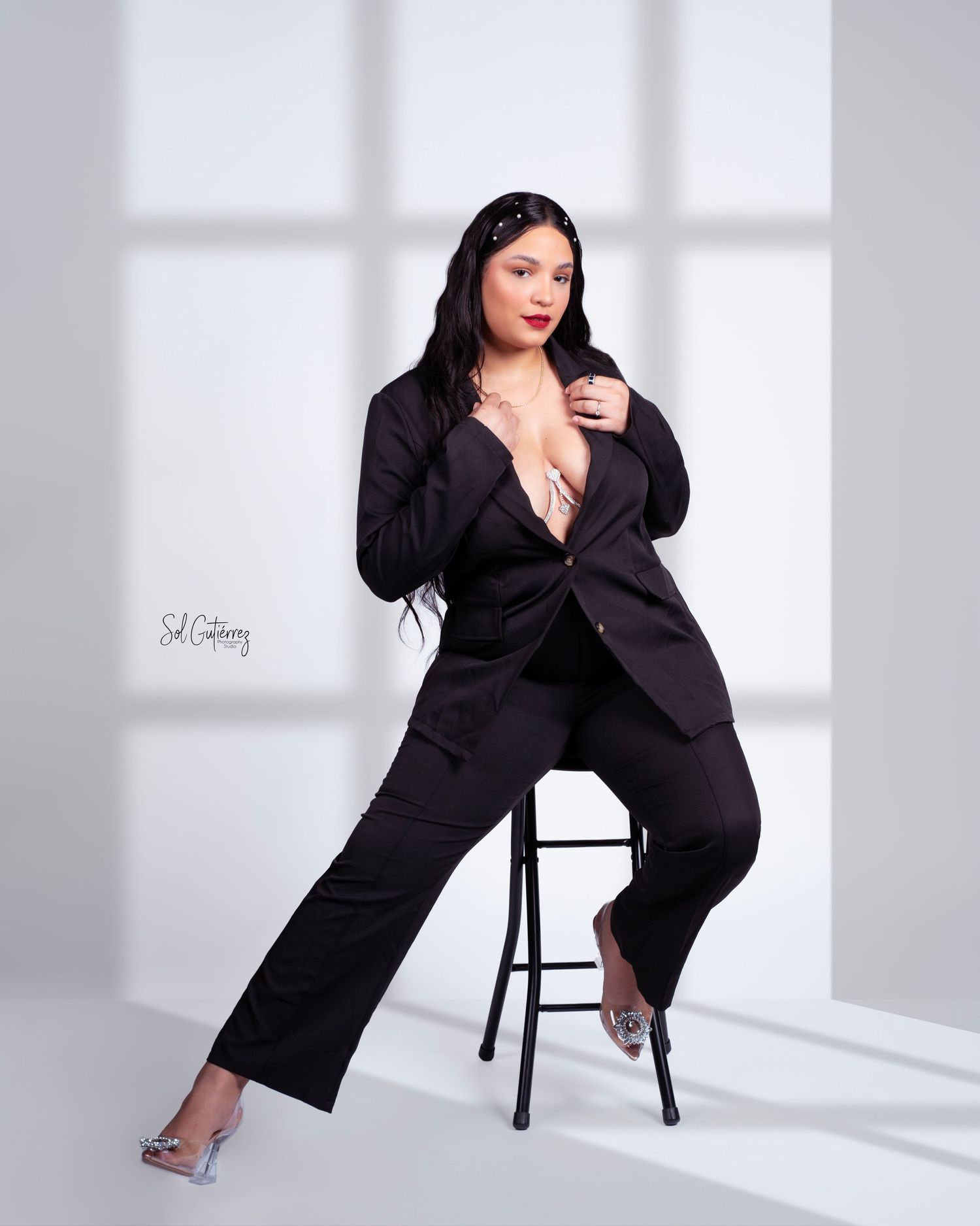 Professional studio portrait in Allentown PA of woman in black suit sitting on stool with soft window light.