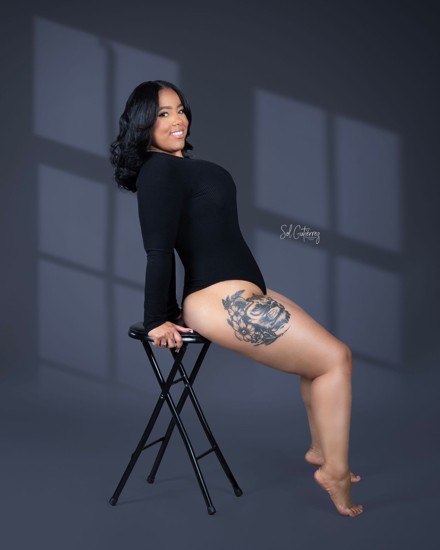 Creative portrait photography in Allentown PA of woman in black bodysuit with thigh tattoo on stool