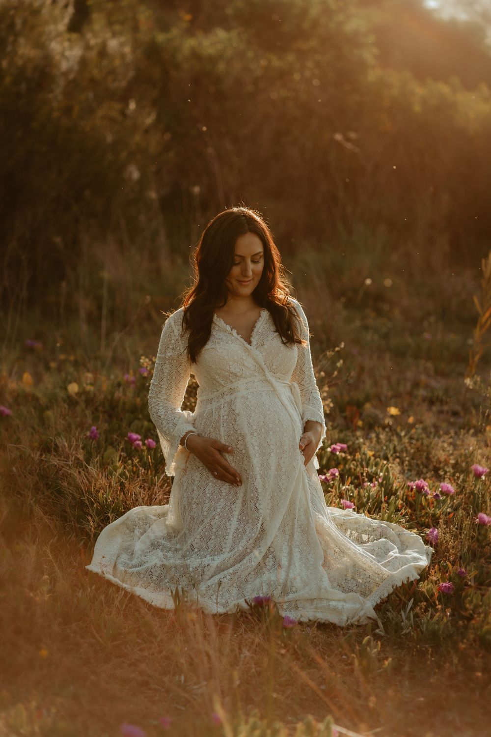 A person in a flowing white dress sits gracefully among wildflowers during golden hour sunset.