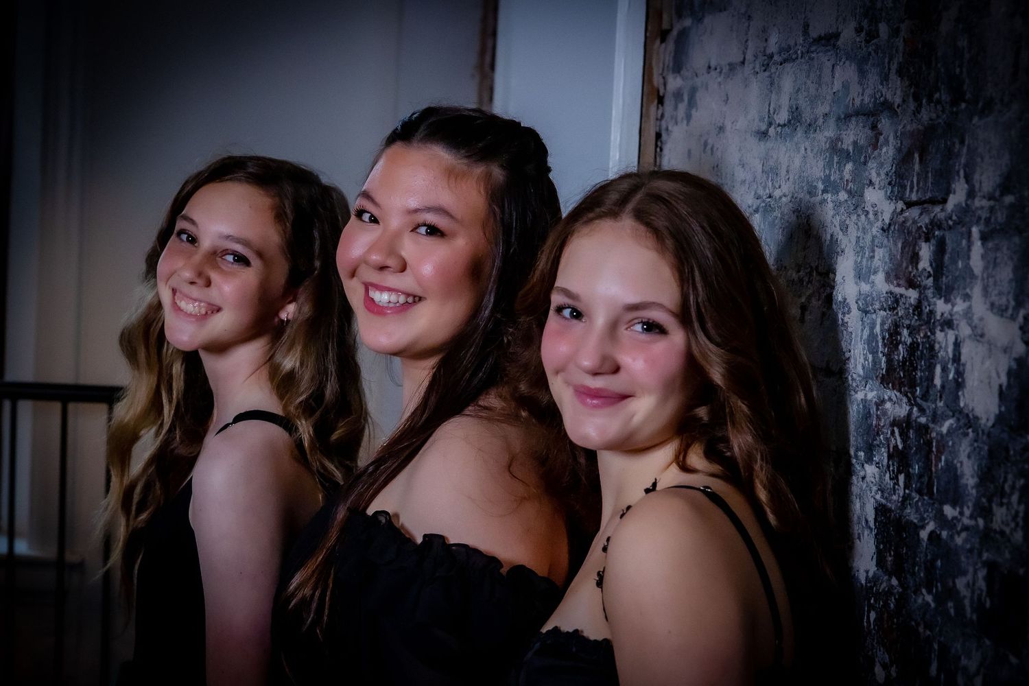 Group poses in coordinated yellow dresses for artistic studio portrait against dark background.