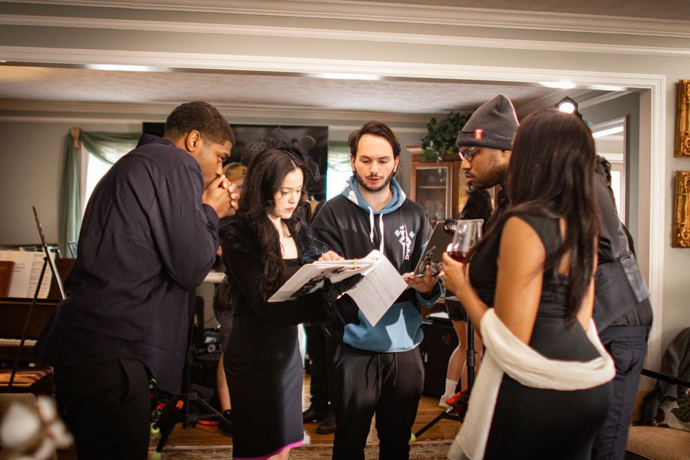 A group of people gather in a studio space reviewing documents and having a creative discussion together.