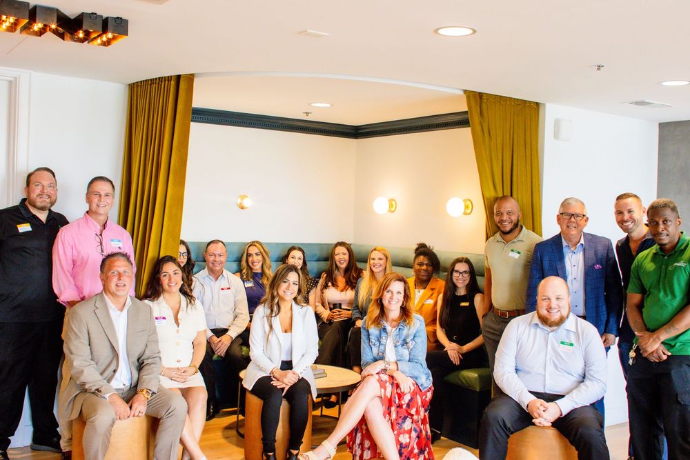 A group of people gather together for a photo in a meeting room with gold curtains and wall sconces.
