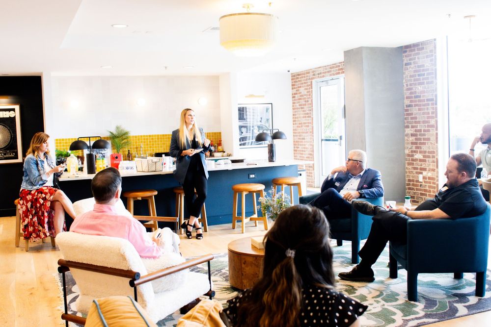 Modern open office workspace with exposed brick walls, shared desks, and natural lighting through large windows.