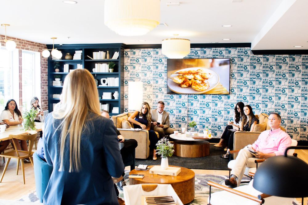 Modern co-working space with people working at desks and meeting areas featuring blue patterned wallpaper and natural light.