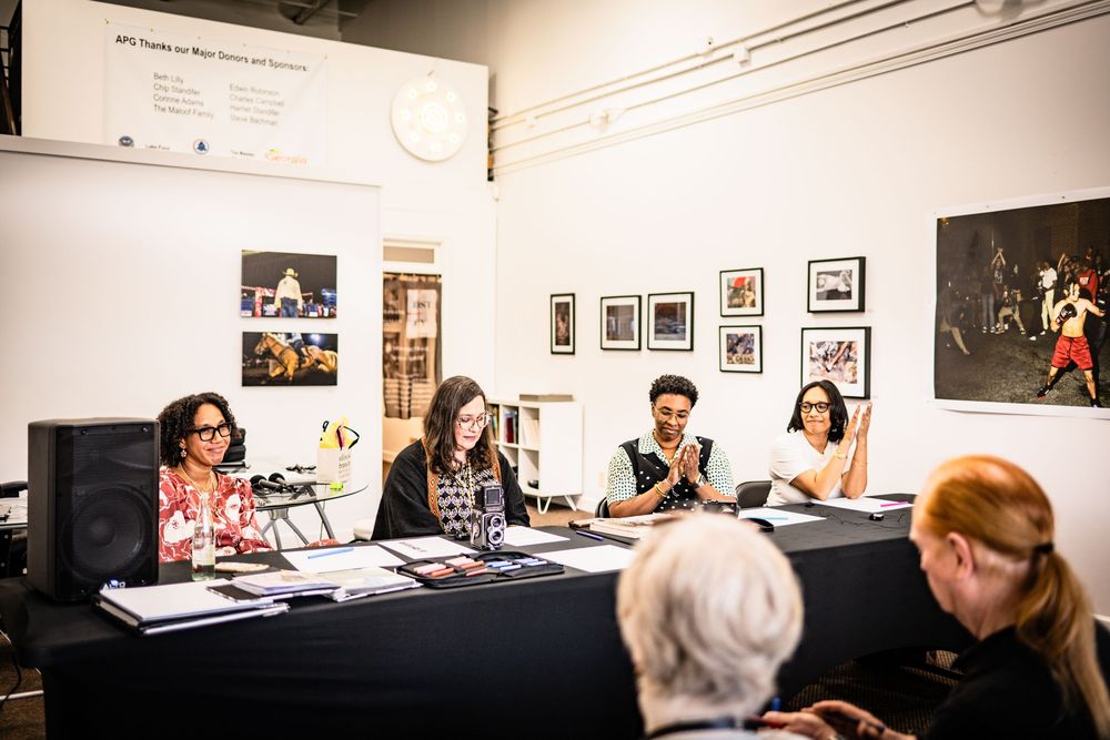 People seated at a long table during a panel discussion in an art gallery with framed photographs on the walls.