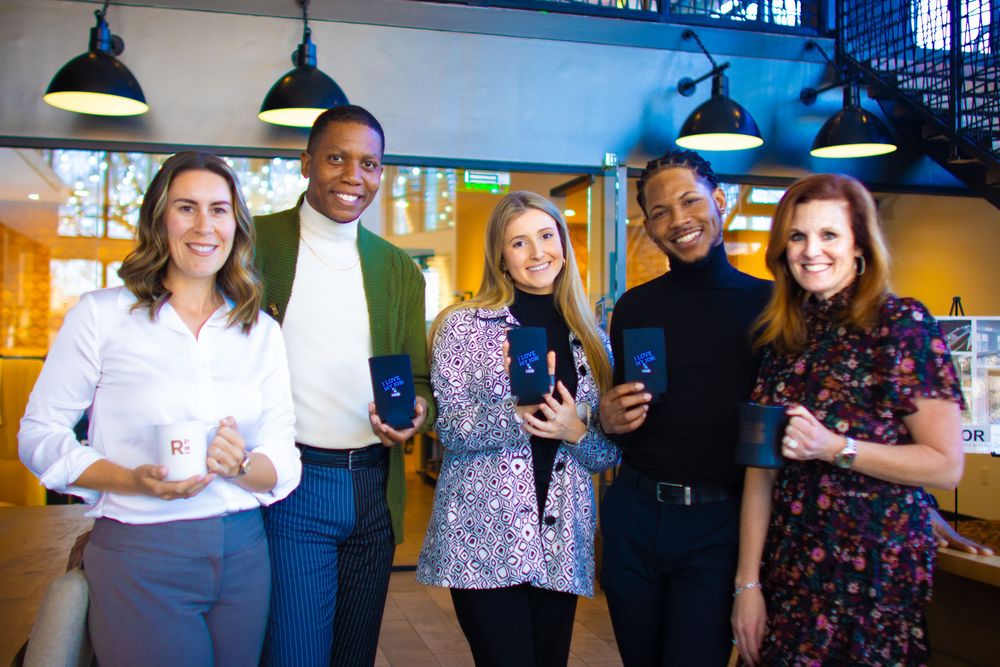 A group of coworkers smile and socialize while holding beverages at a casual office gathering.