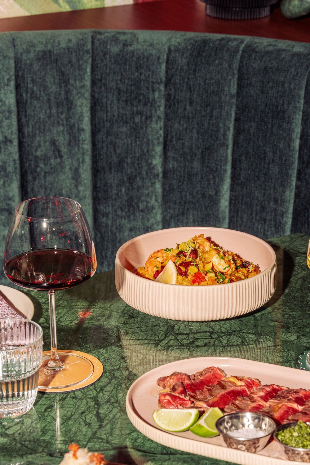 Elegant dinner table setting with wine glasses, plates of food, and moody lighting against a dark wooden fence backdrop.