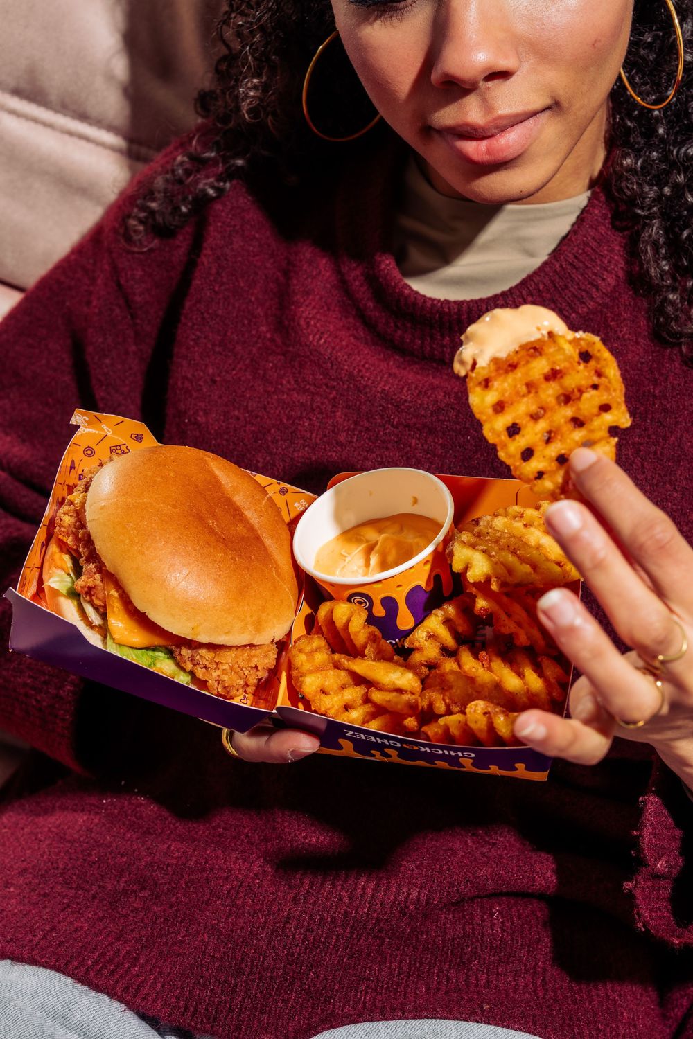 Person in burgundy sweater eating a burger and waffle fries in a sequence of close-up shots.