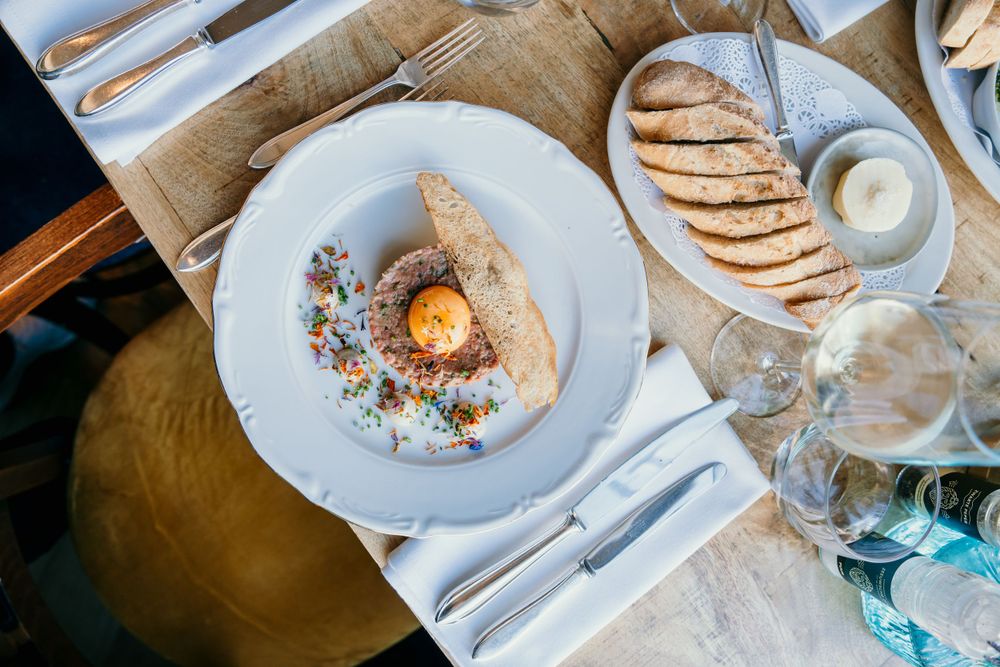 Gourmet dish with soft-boiled egg and garnish served on white plate with bread basket.