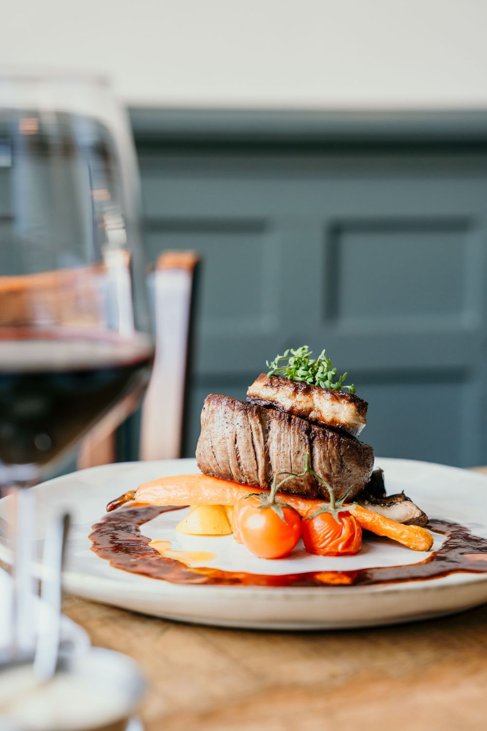 Beautifully plated filet mignon with roasted vegetables and a red wine sauce on a white plate.