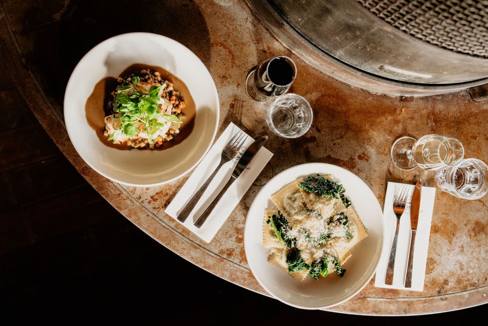 Overhead view of two elegant dishes served on a round table with wine glasses.