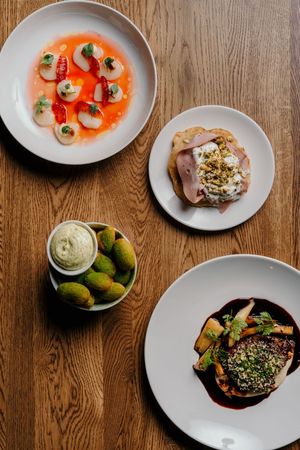 A series of elegantly plated dishes on white plates arranged on a rustic wooden table showcasing fine dining cuisine.