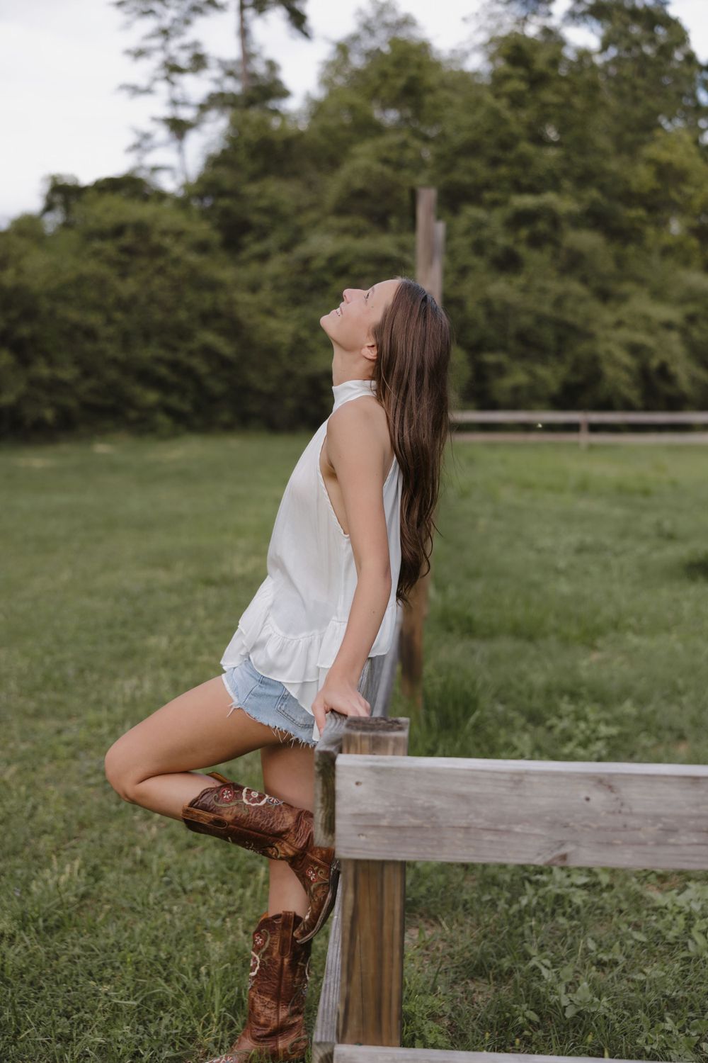 A countryside portrait featuring western boots, denim shorts and a white top against a rustic wooden fence.