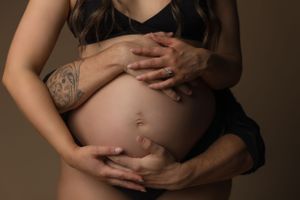 Intimate maternity photo showing hands gently cradling a pregnant belly in warm lighting against dark clothing.