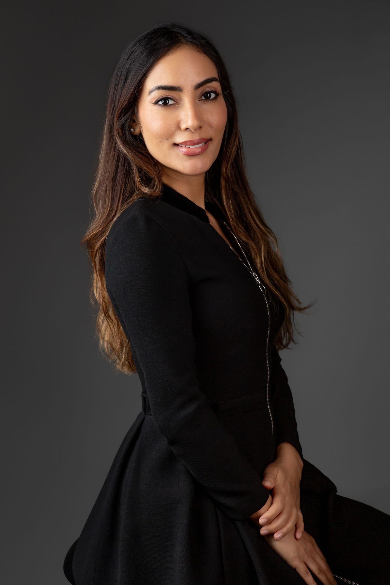A professional portrait of a woman in a black outfit, standing confidently with her arms crossed against a dark studio background