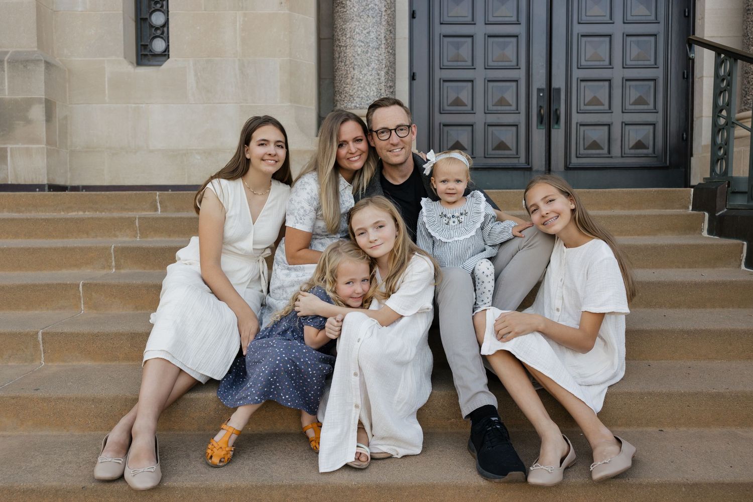 Group wearing white outfits sitting together on stone steps in front of blue doors.