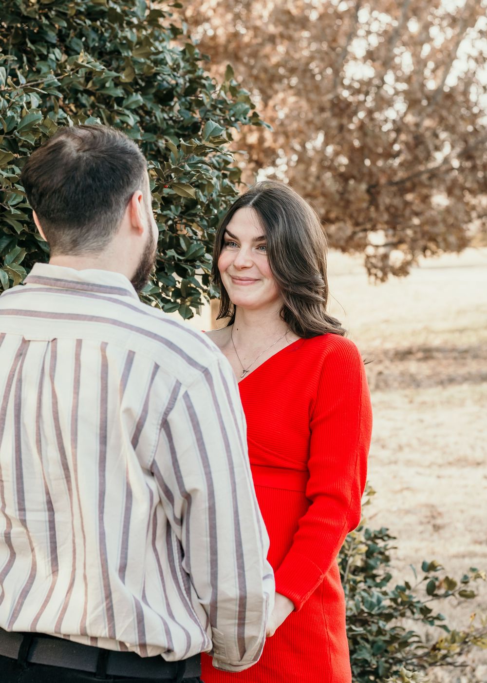 A couple in autumn colors shares a romantic moment outdoors, with the woman in red standing out against fall foliage.