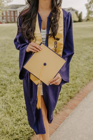 A close-up of graduation regalia showing a gold tassel and diploma against purple graduation gown.