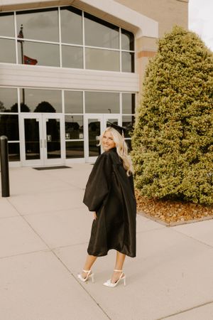 Woman in black coat and heels walking past modern building exterior.