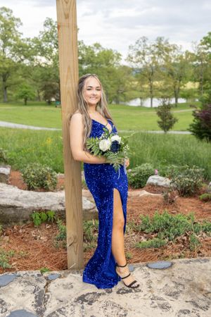 A sparkling blue formal dress and floral bouquet photographed outdoors with a scenic lake backdrop.