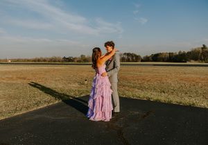 Couple in formal attire poses together on rural road during sunset.