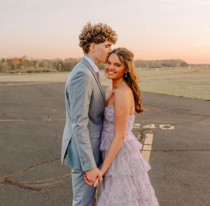 Couple in formal wear shares romantic moment on airfield at sunset.