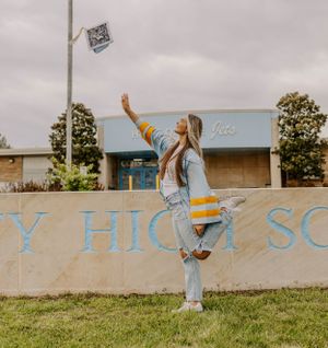 Graduate tosses cap in air while wearing light blue graduation gown outside high school.
