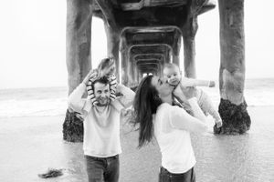 A family of four laughing under a pier at the beach in black and white