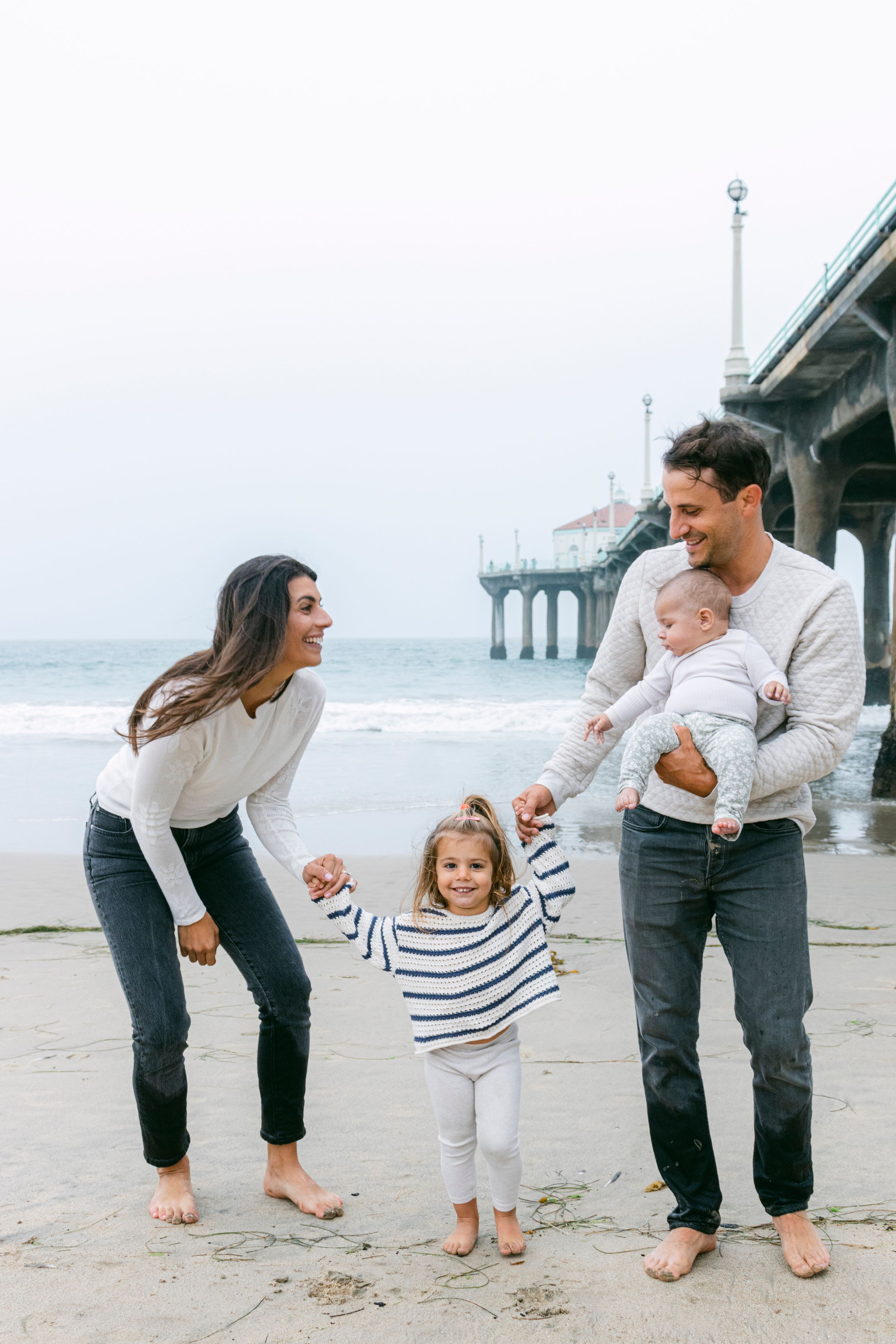 A family of four running and laughing on the beach on an overcast day
