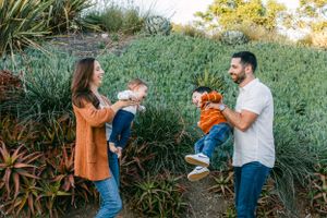 A family of four (mother, daughter, son and father, playfully holding their children in front of succulents in southern california