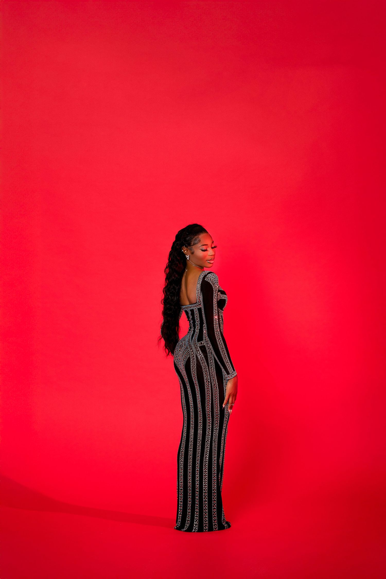 Fashion portrait on red backdrop featuring sleek black striped evening gown.