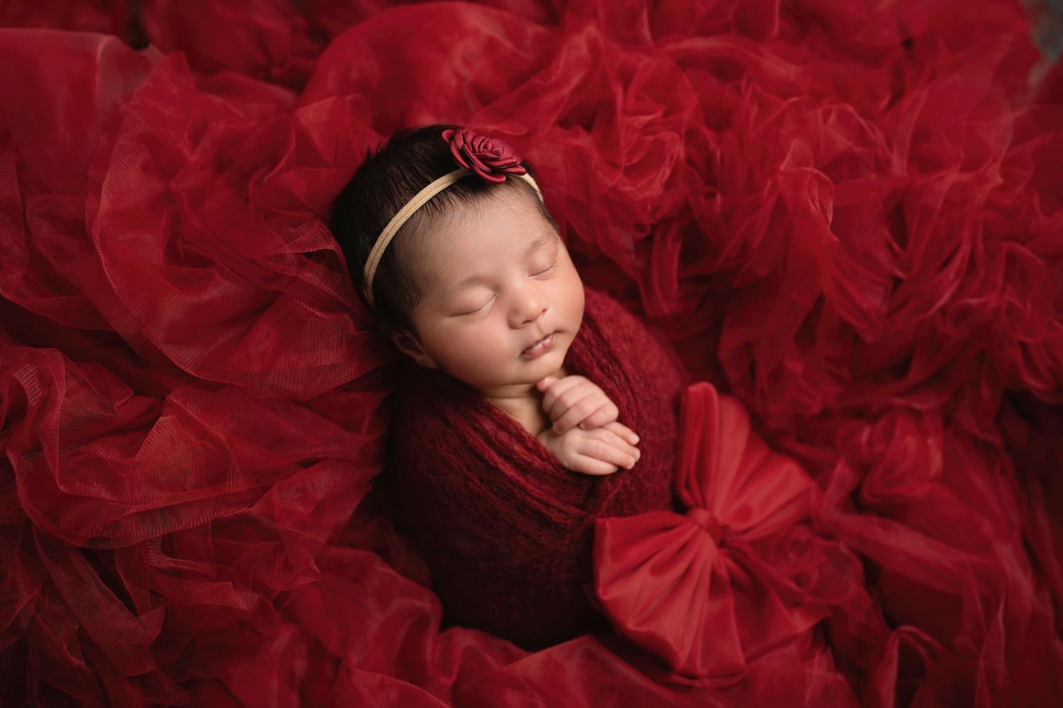 Newborn baby peacefully sleeping on red tulle fabric in artistic portrait session.