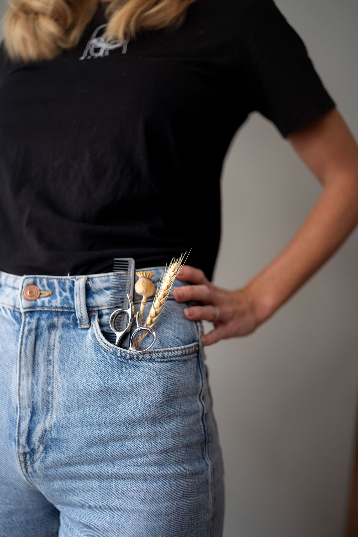 Closeup of hair styling scissors tucked into the front pocket of light wash high waisted jeans with a black t-shirt.