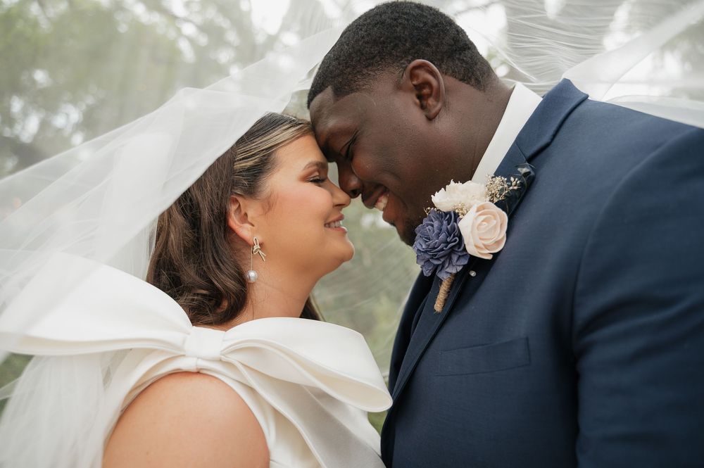 A joyful couple in wedding attire share an intimate moment together outdoors with a white rose boutonniere.