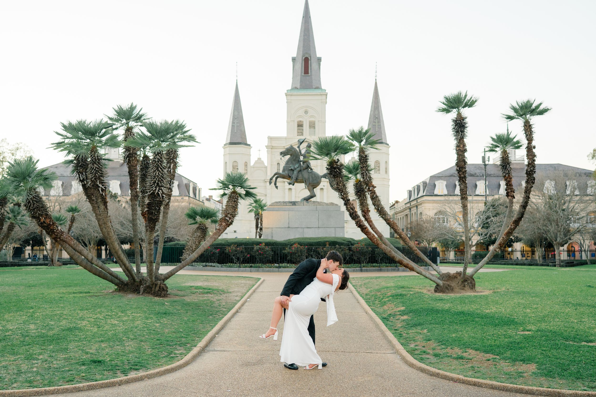 Couple sharing a romantic dip kiss in Jackson Square, New Orleans, with St. Louis Cathedral and palm trees in background.