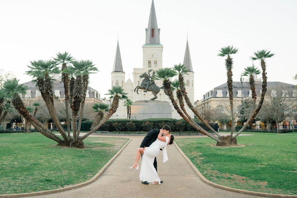Couple sharing a romantic dip kiss in Jackson Square, New Orleans, with St. Louis Cathedral and palm trees in background.