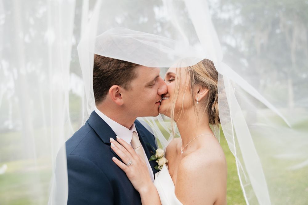 A bride and groom share a tender kiss under a flowing white veil on their wedding day.