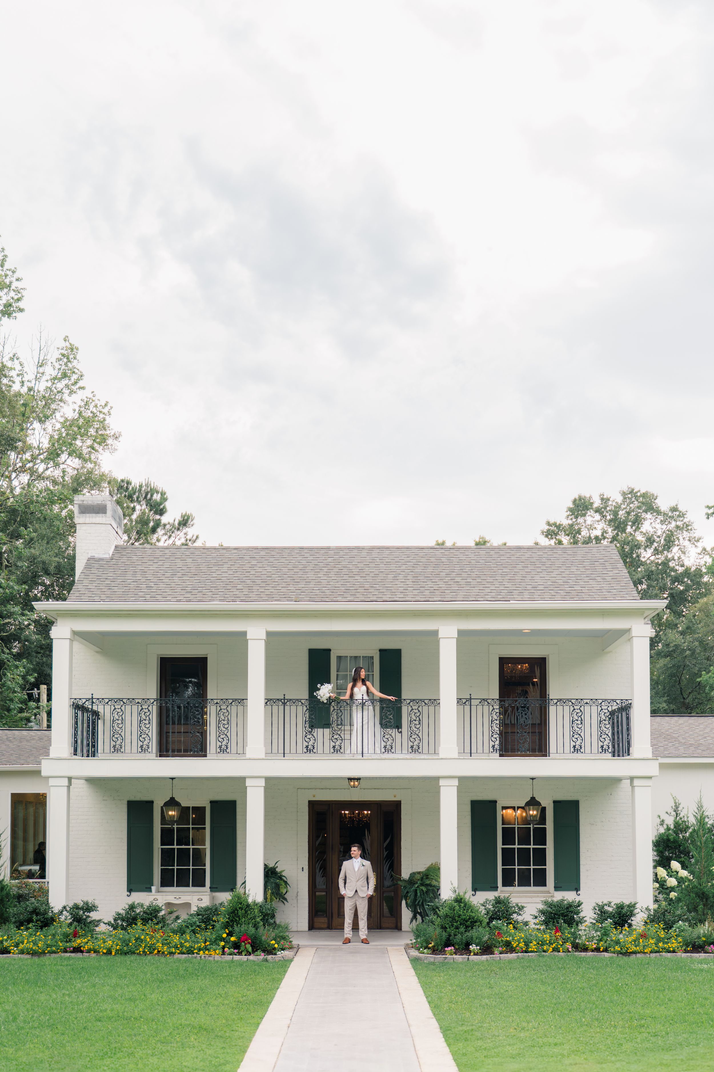 Bride and groom pose outside a white Southern colonial wedding venue with green shutters and wraparound balcony.