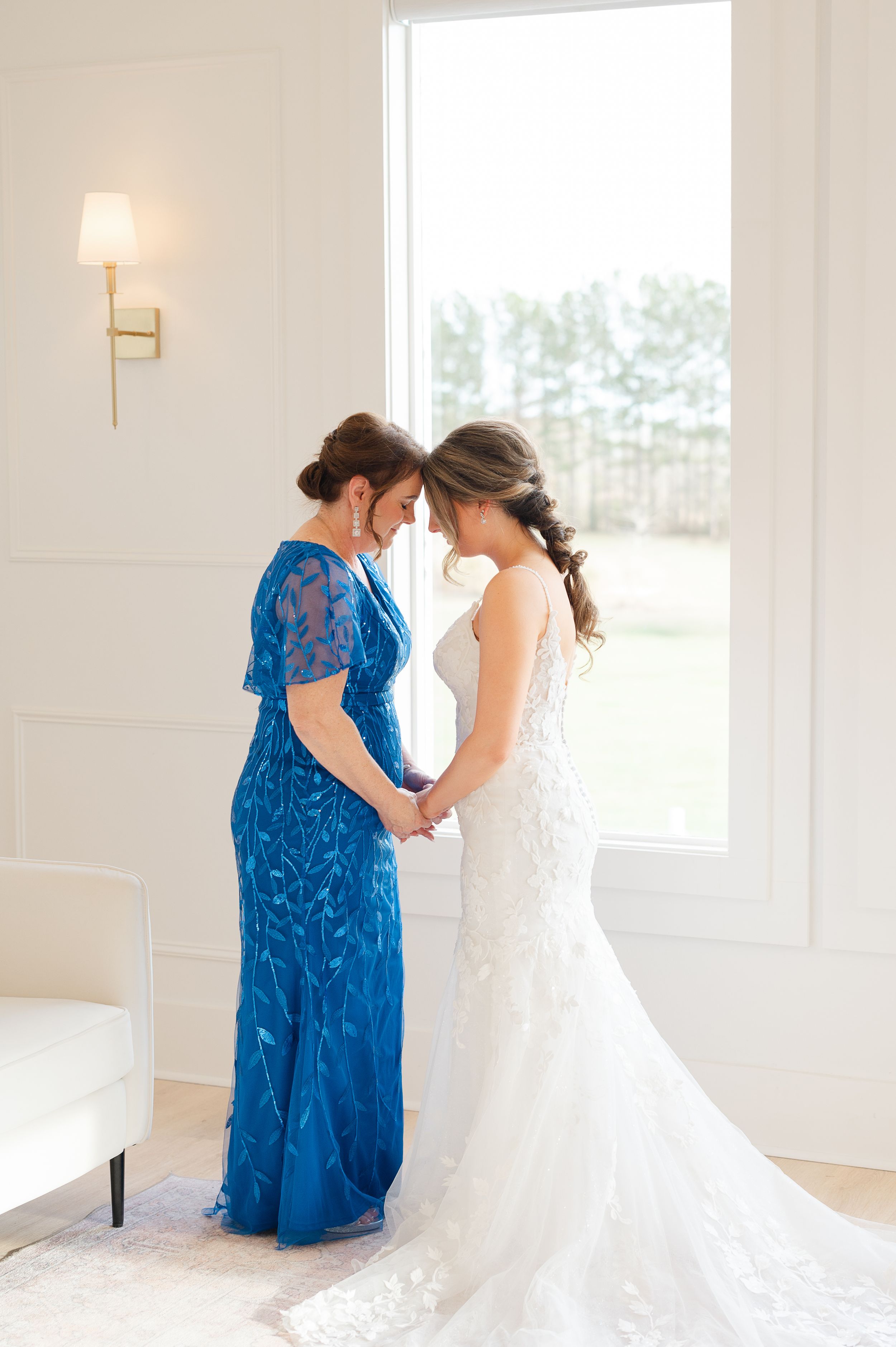 Two figures share an intimate moment in formal attire, with one wearing a royal blue gown and another in white lace wedding dress.