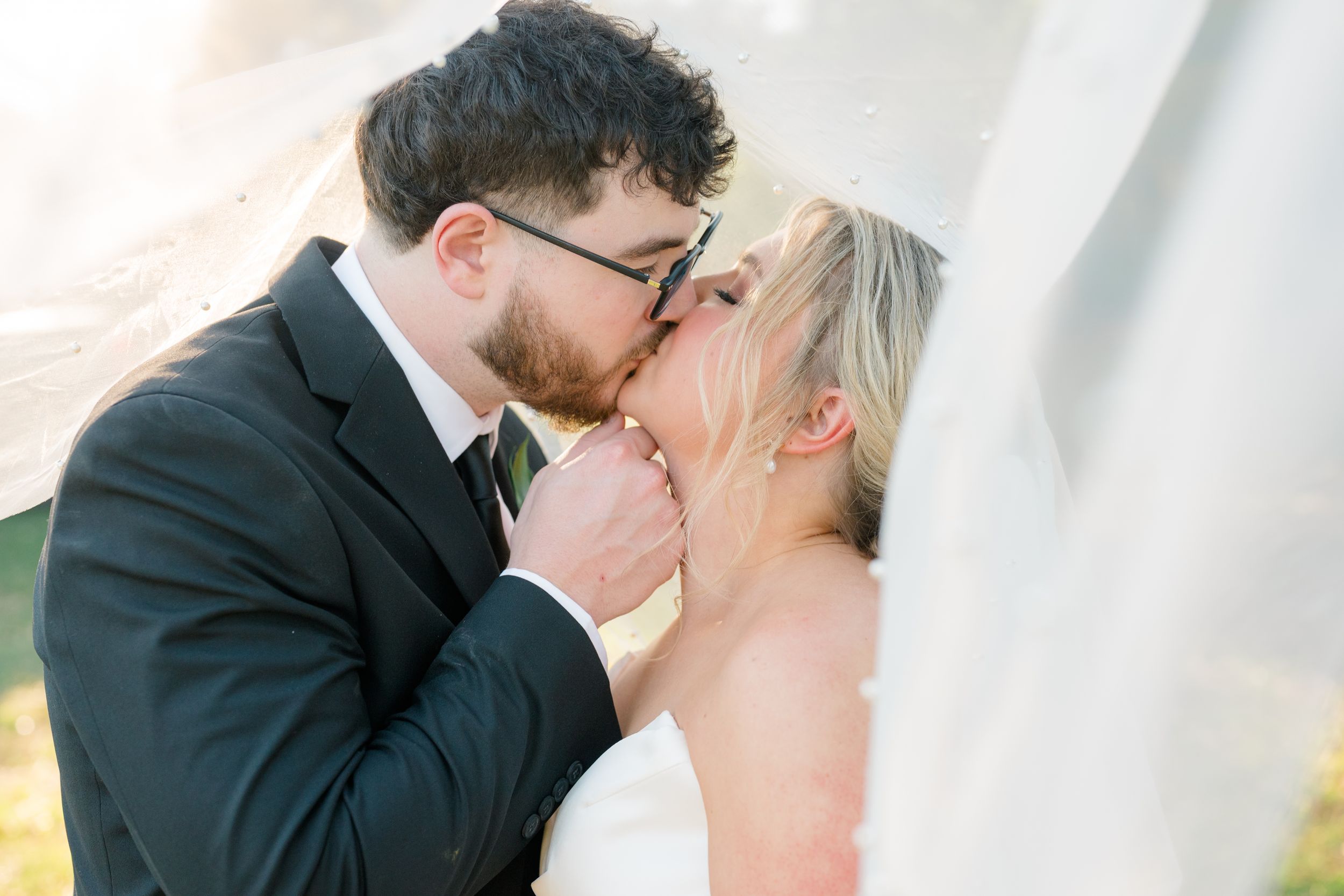 A bride and groom share a romantic kiss under a flowing white veil on their wedding day.