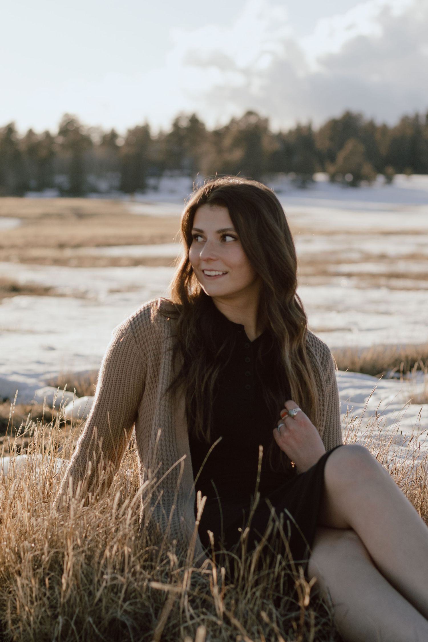 A person sits in a winter field wearing a sweater during golden hour.