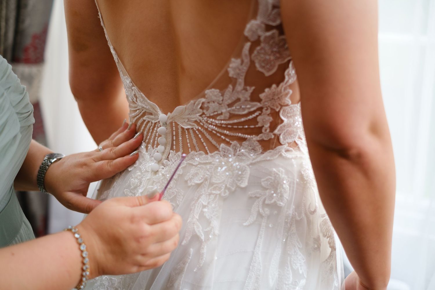 Bride having her beautiful lace dress fastened by her bridesmaid