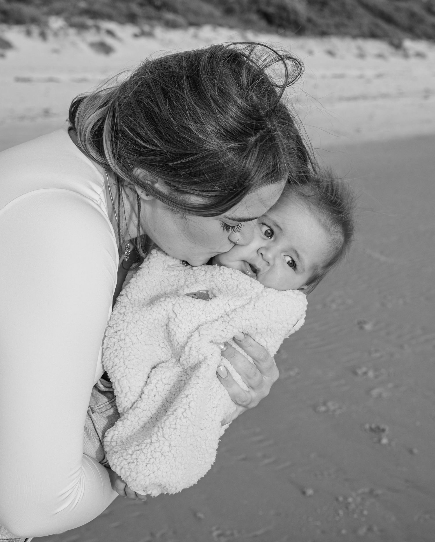 Woman in white dress holding baby in matching white outfit in sunny field.