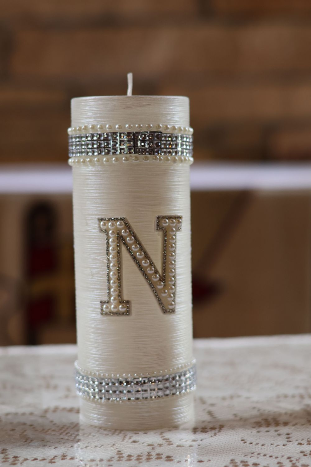 Decorative white pillar candle with rhinestone accents and monogram letter N.