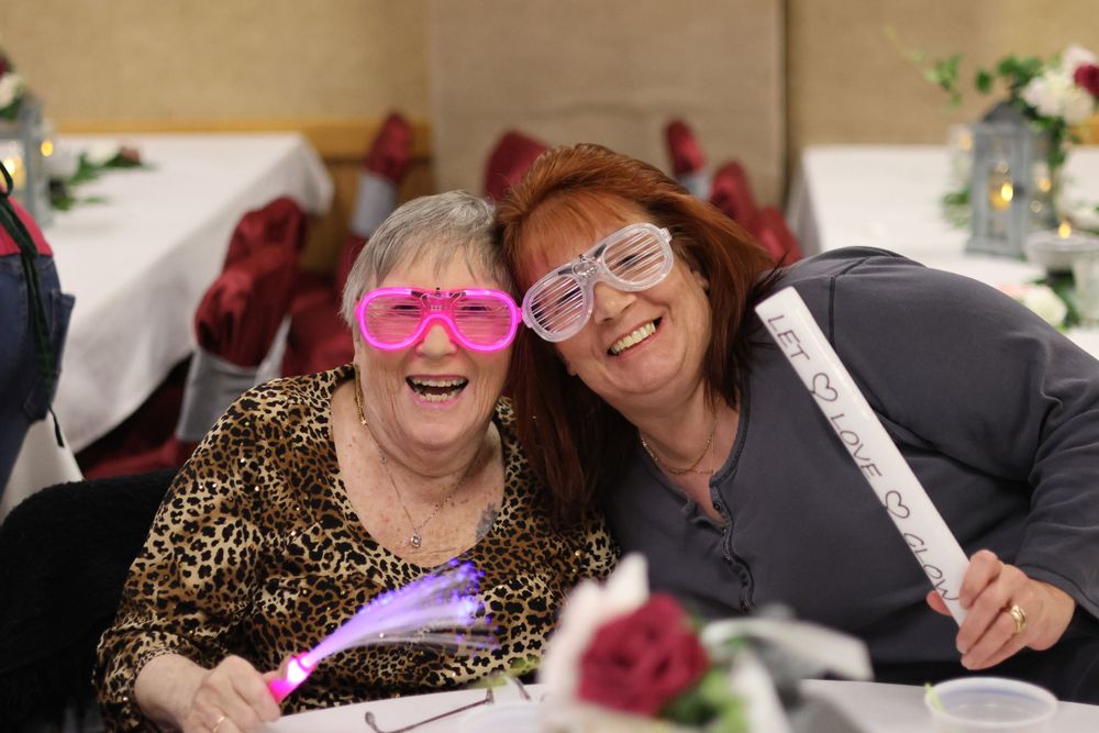 Two party guests wearing fun novelty glasses share a joyful moment at a celebration.