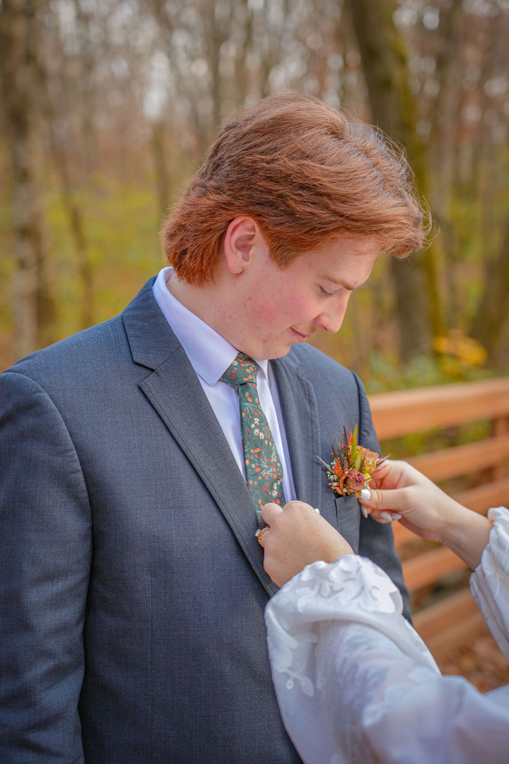 Wedding boutonniere being pinned to groom's lapel on wooden deck.