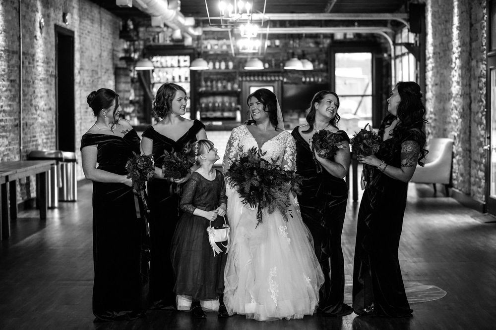Black and white wedding party poses under illuminated archway at night creating a romantic silhouette effect.
