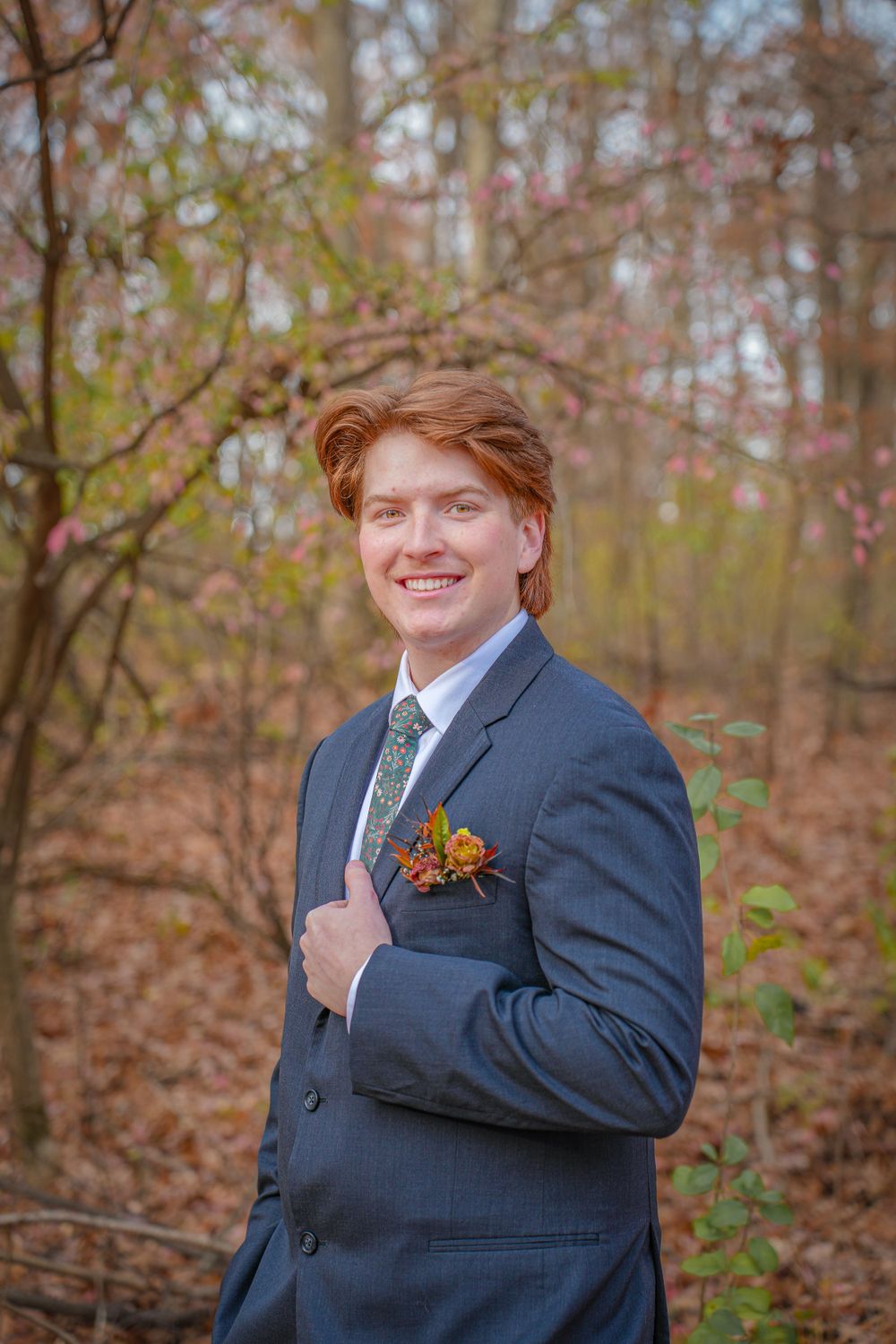 Groom in navy suit with orange boutonniere smiles during autumn wedding photoshoot.