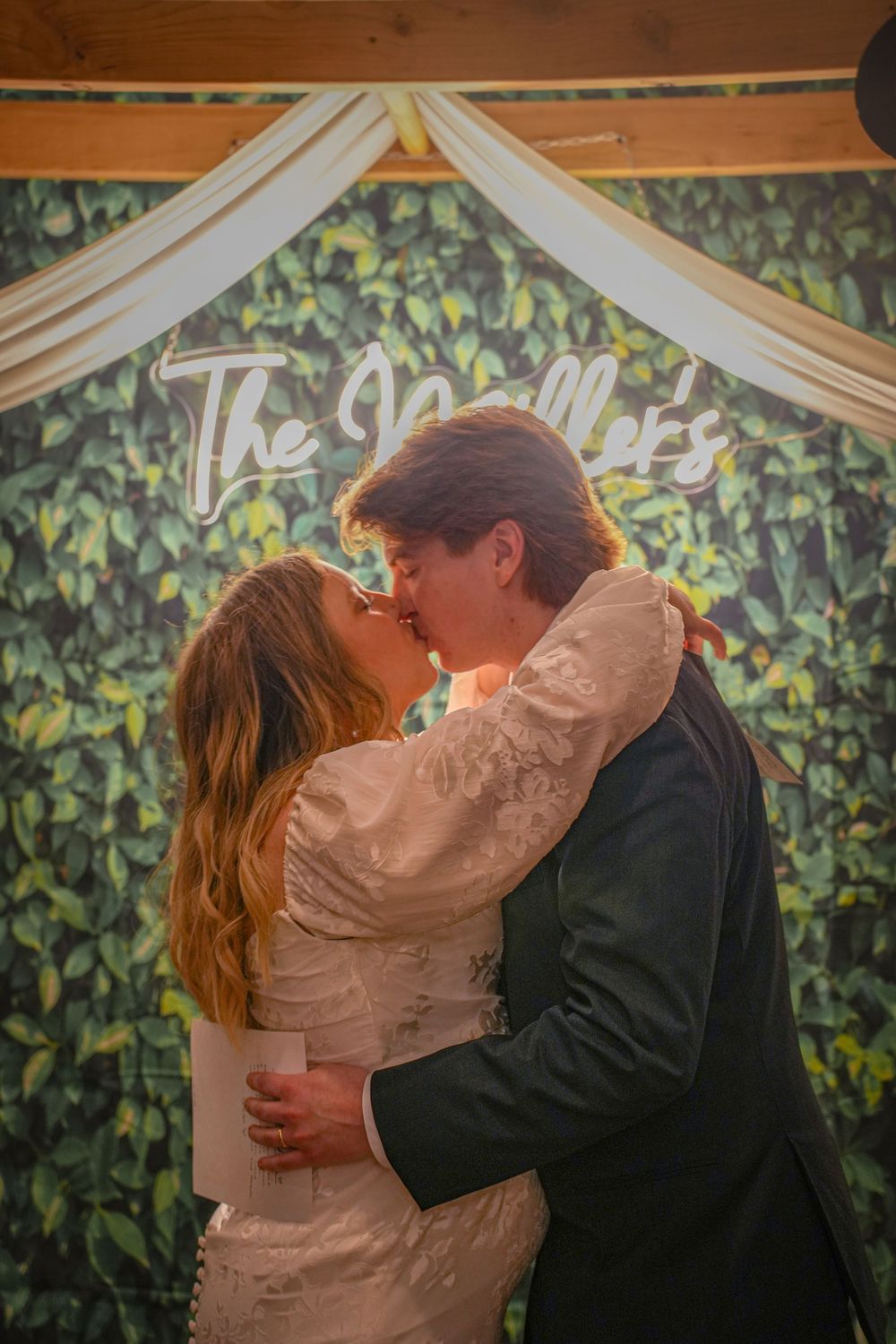 Romantic kiss under draped fabric wedding arch with greenery backdrop.